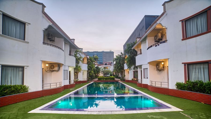 A symmetrical view of Ilara Hotels & Spa, OMR, Chennai with red roofs, flanking a long, narrow swimming pool or water feature, bathed in daylight.