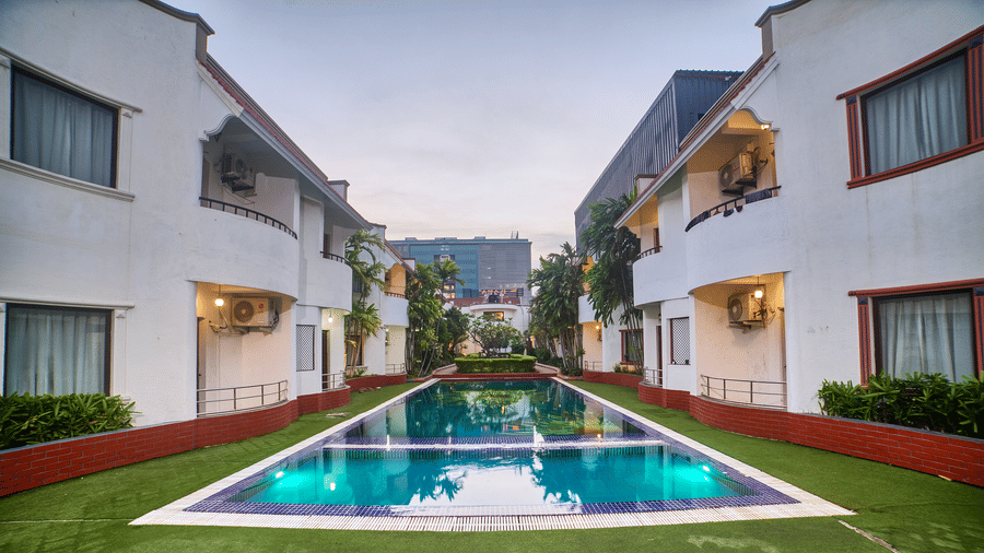 A symmetrical view of Ilara Hotels & Spa, OMR, Chennai with red roofs, flanking a long, narrow swimming pool or water feature, bathed in daylight.