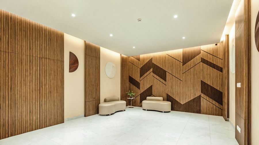 A pre-function area at Mango Hill Central, Chennai, with modern wooden wall panels, a tiled floor, and two small seating benches.