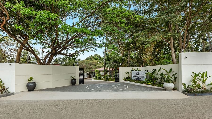 The illuminated entrance to Mango Hill Resort, Coimbatore, featuring a white gate, a sign, and trees at night