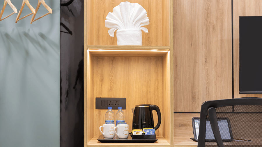 A wooden desk and shelf area featuring an electric kettle, water bottles, and an office chair at Monday Hotels & Suites Madhapur Hyderabad.