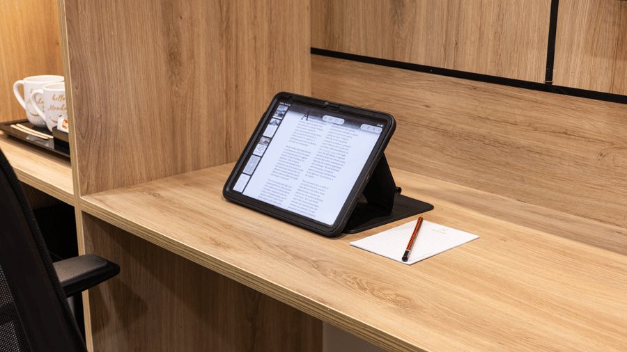 A wooden desk featuring a tablet computer resting on a stand, a notepad with a pen, and an office chair at Monday Hotels & Suites Madhapur Hyderabad.