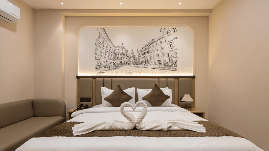 A bedroom with a king size bed with towel art arrangements and a sofa near a wall mural at Monday Hotels & Suites Madhapur Hyderabad.