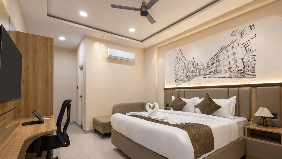 A bedroom featuring a king size bed with towel art, a desk with an office chair, wall-mounted TV, and a wall illustration at Monday Hotels & Suites Madhapur Hyderabad.