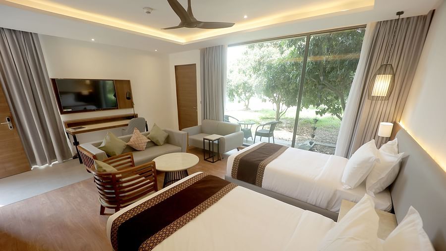 Bright twin room with flat-screen TV, dual chairs, and a view of green lawns through large windows at Wyndham Garden.