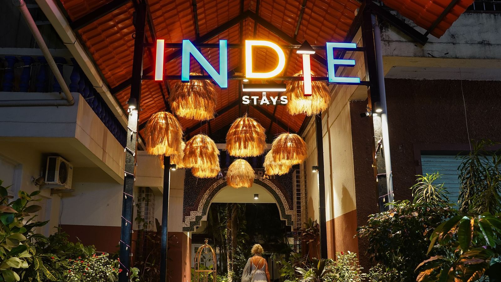 The entrance of Indie Stays features inviting hanging lights and plants on either side, creating a warm and welcoming atmosphere
