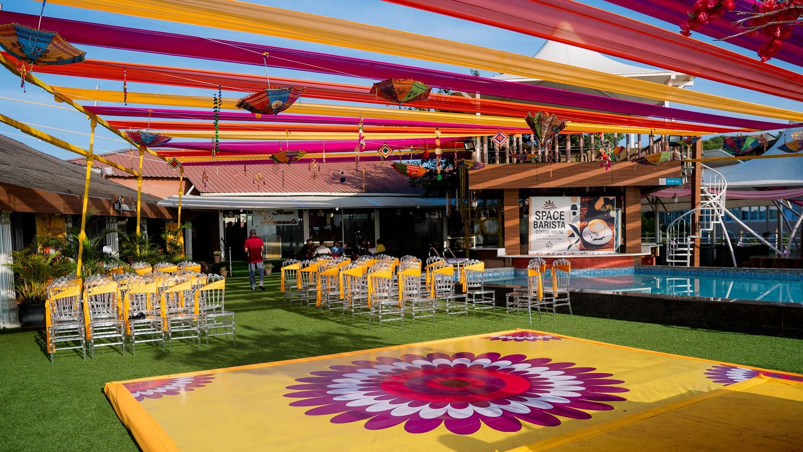 A colourful wedding venue with a patterned dance floor, draped fabrics overhead, and set tables, suggesting a lively reception setting - The Grand Legacy Resort and Spa