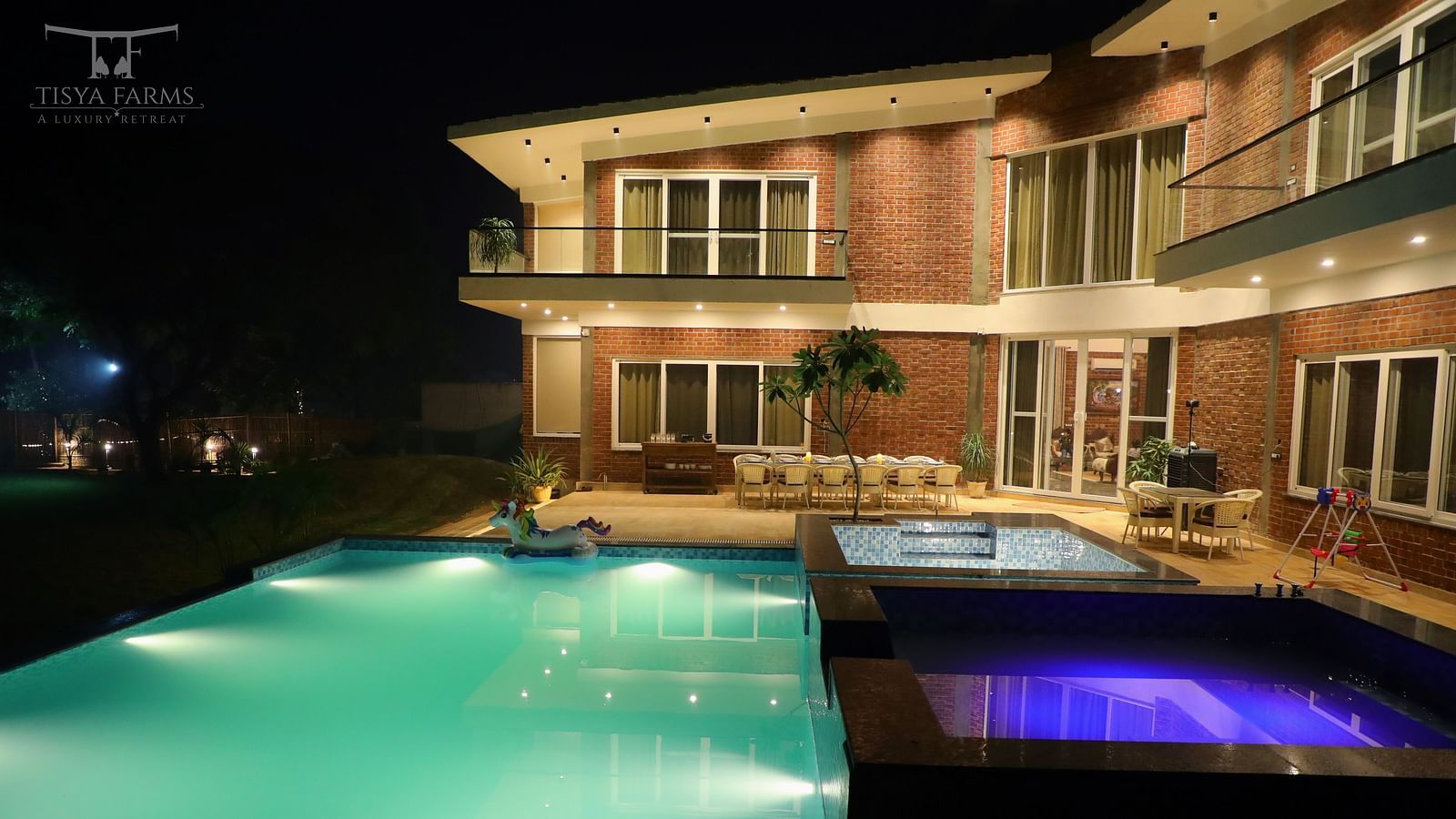A night view of a farmhouse with an illuminated swimming pool in front at Tisya Farms, Gurgaon.