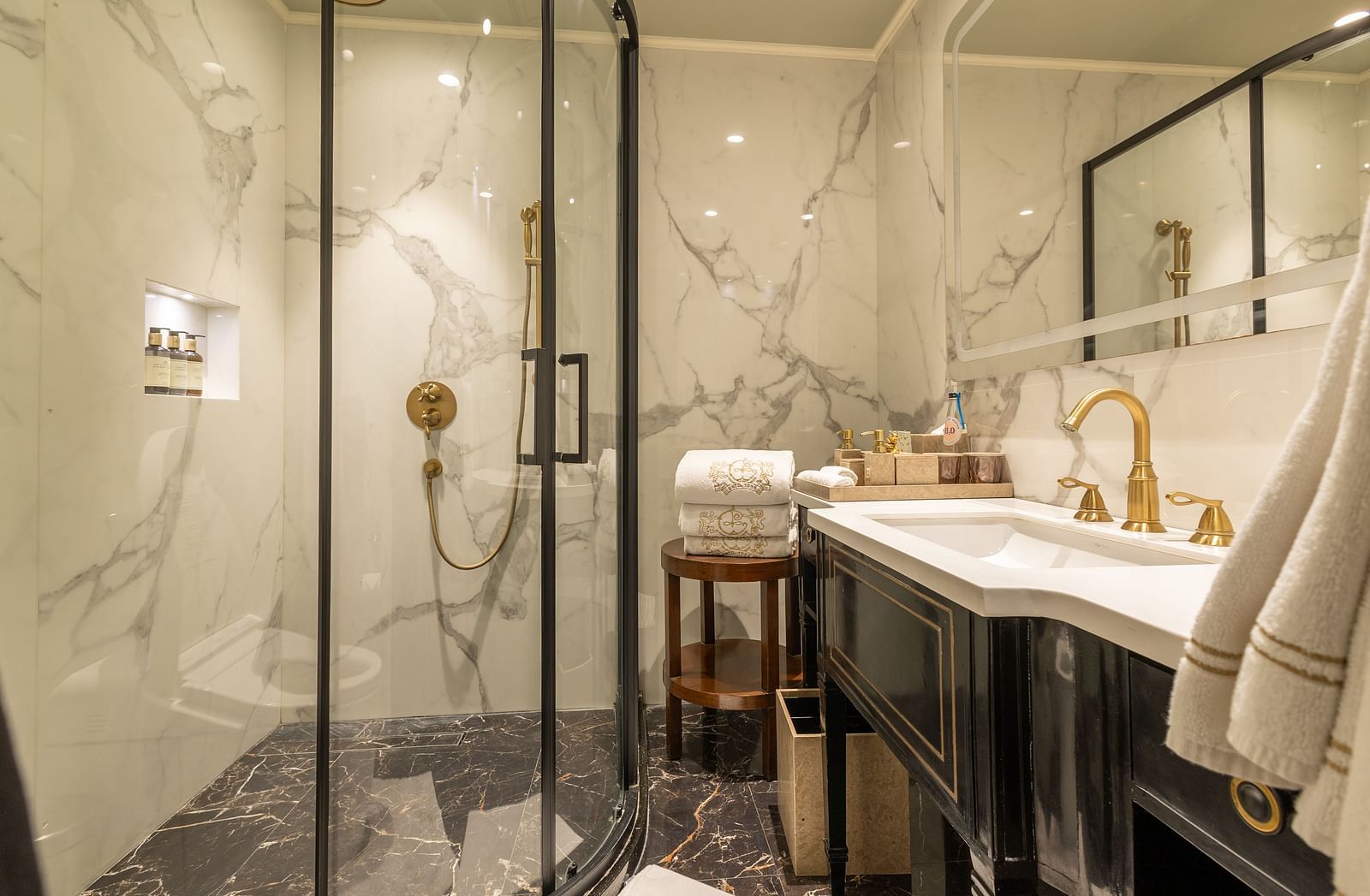 Luxury Suite with Whirlpool washroom at The Claridges New Delhi, featuring a sleek sink, wall-mounted mirror, and a glass-enclosed bath area