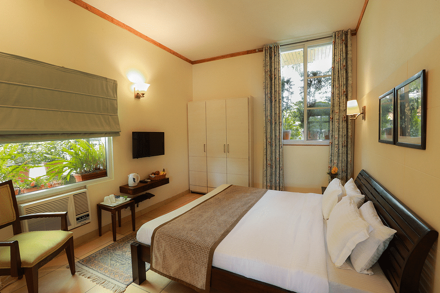Full angle view of deluxe room with a large window facing the landscape along with room amenities like a television, a wardrobe, etc. - Lamrin Norwood Green, Palampur