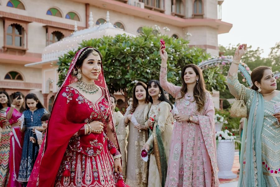 The bride walks through a crowd of women, all in traditional attire, with some holding flower petals in the air - Umaid Palace - Best Luxury Heritage Resort Near Jaipur 