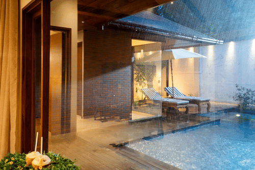 Pool villa at Uday Backwater Resort with a private pool, wooden deck, lounge chairs, and warm ambient lighting during a rainy evening
