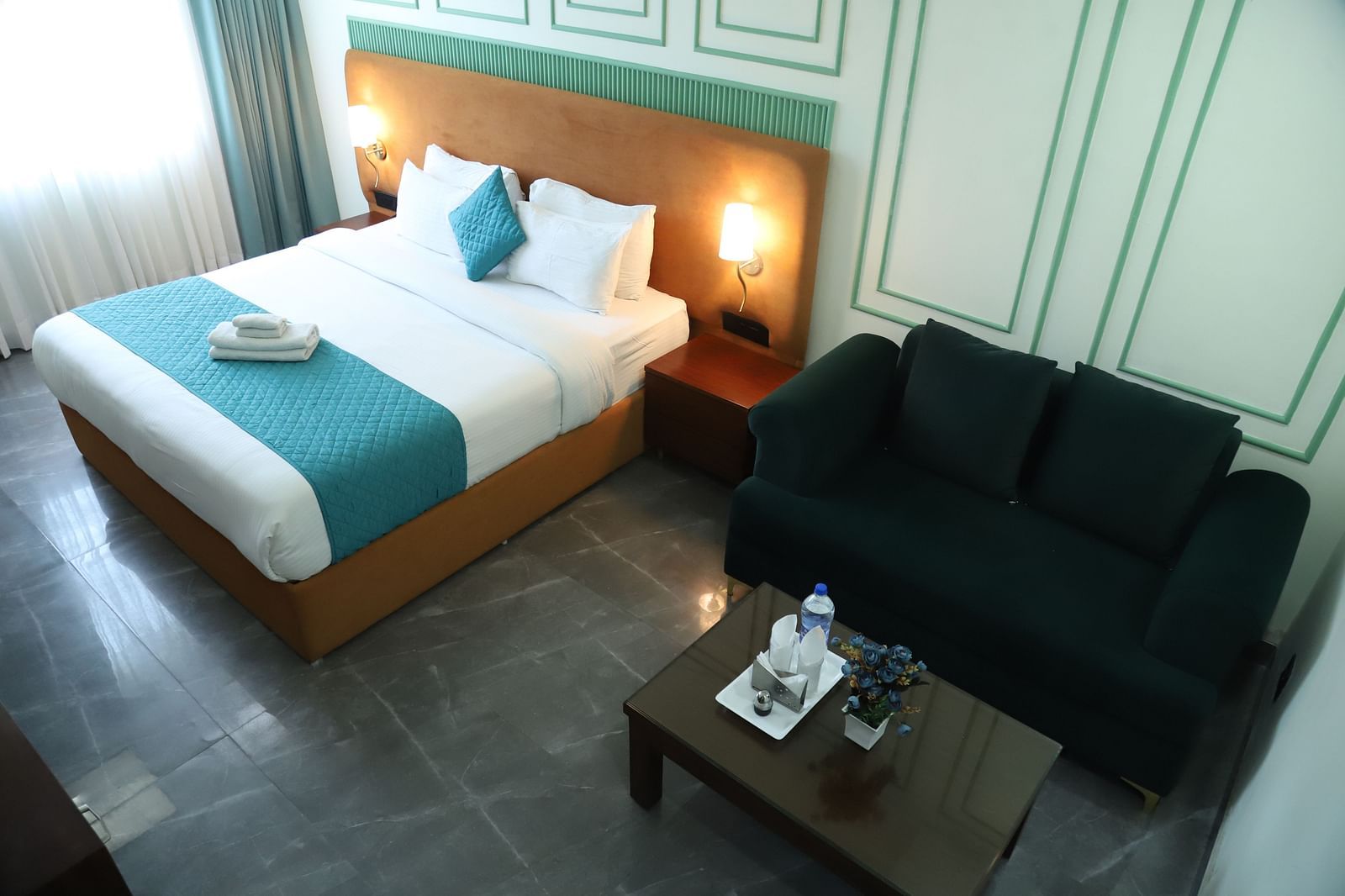 A room with a double bed featuring a blue and white design, alongside a dark coloured sofa - Asian Suites IFFCO Metro, Gurgaon