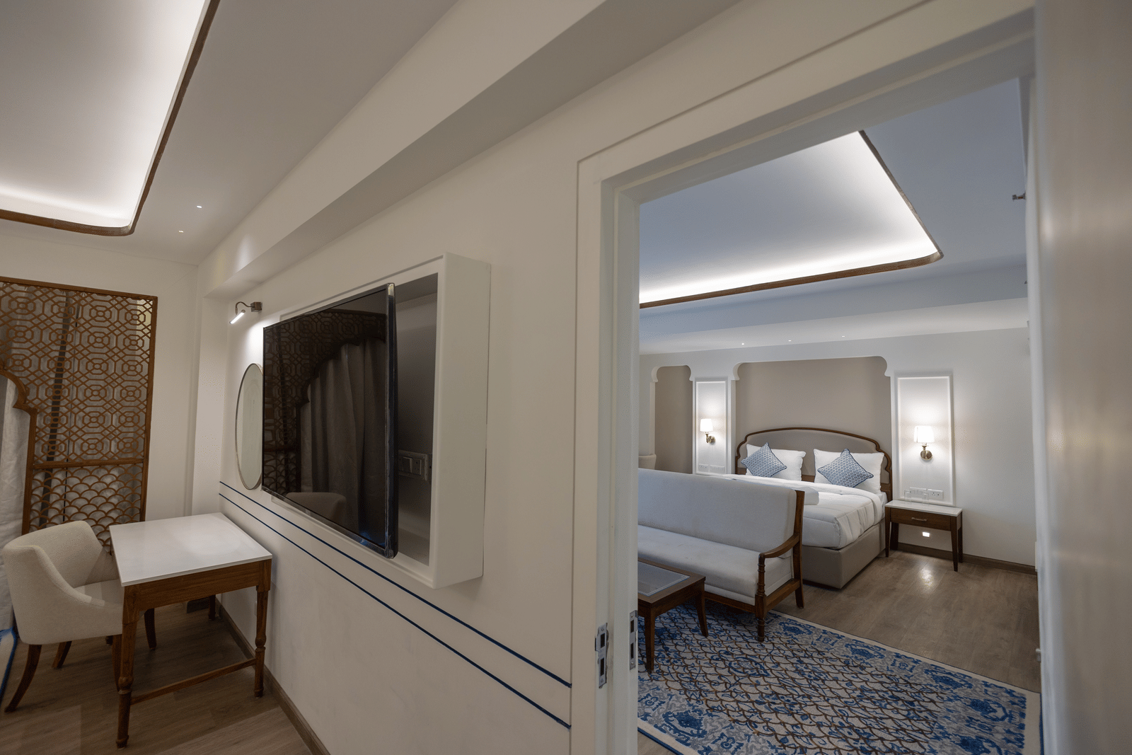 Ananta Room at Bhagirathi by Atishay with a workspace under soft lighting, and a view into a bedroom featuring a large bed and patterned rug