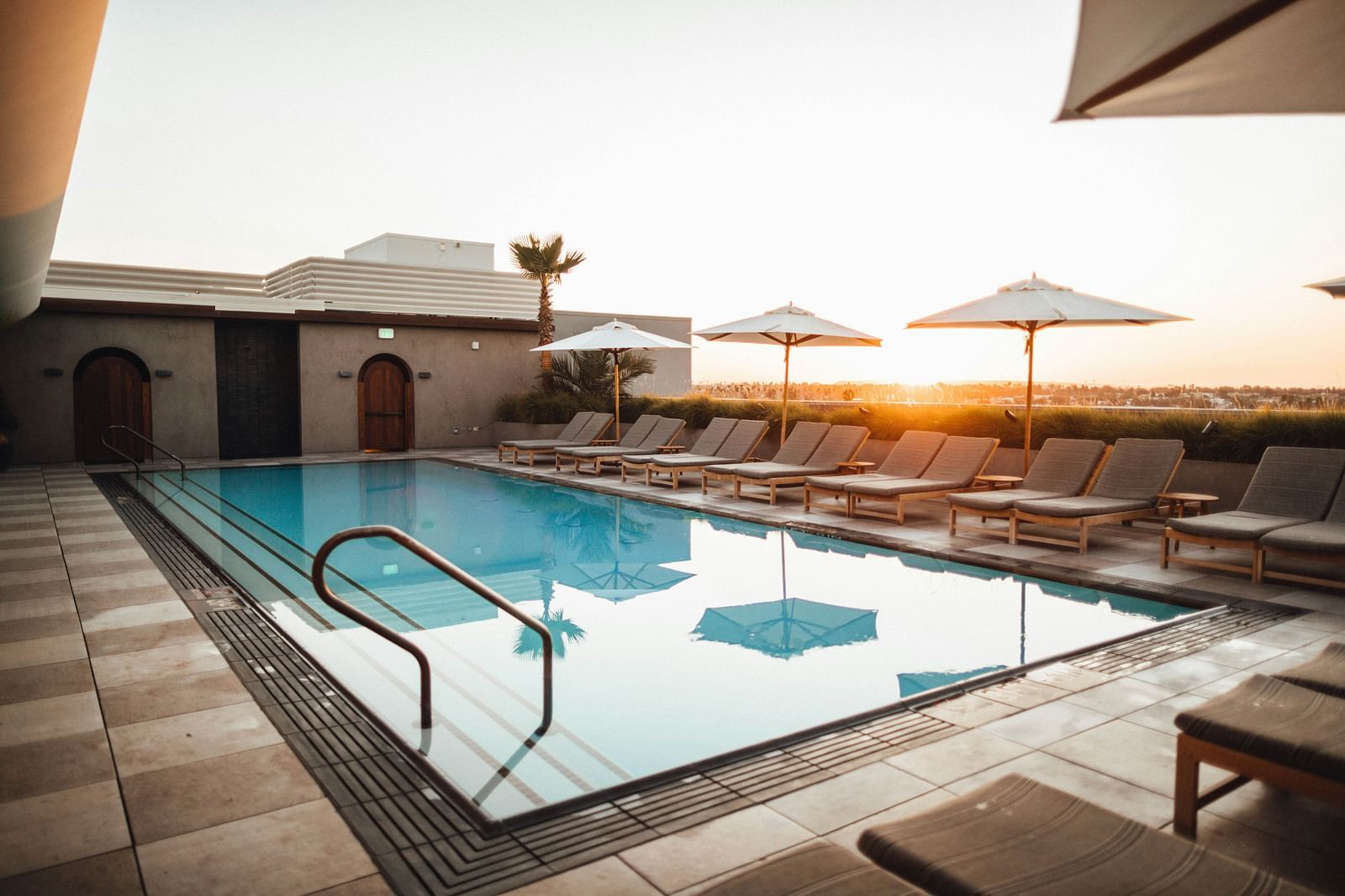 An image of a swimming pool featuring sun loungers seen during a sunset