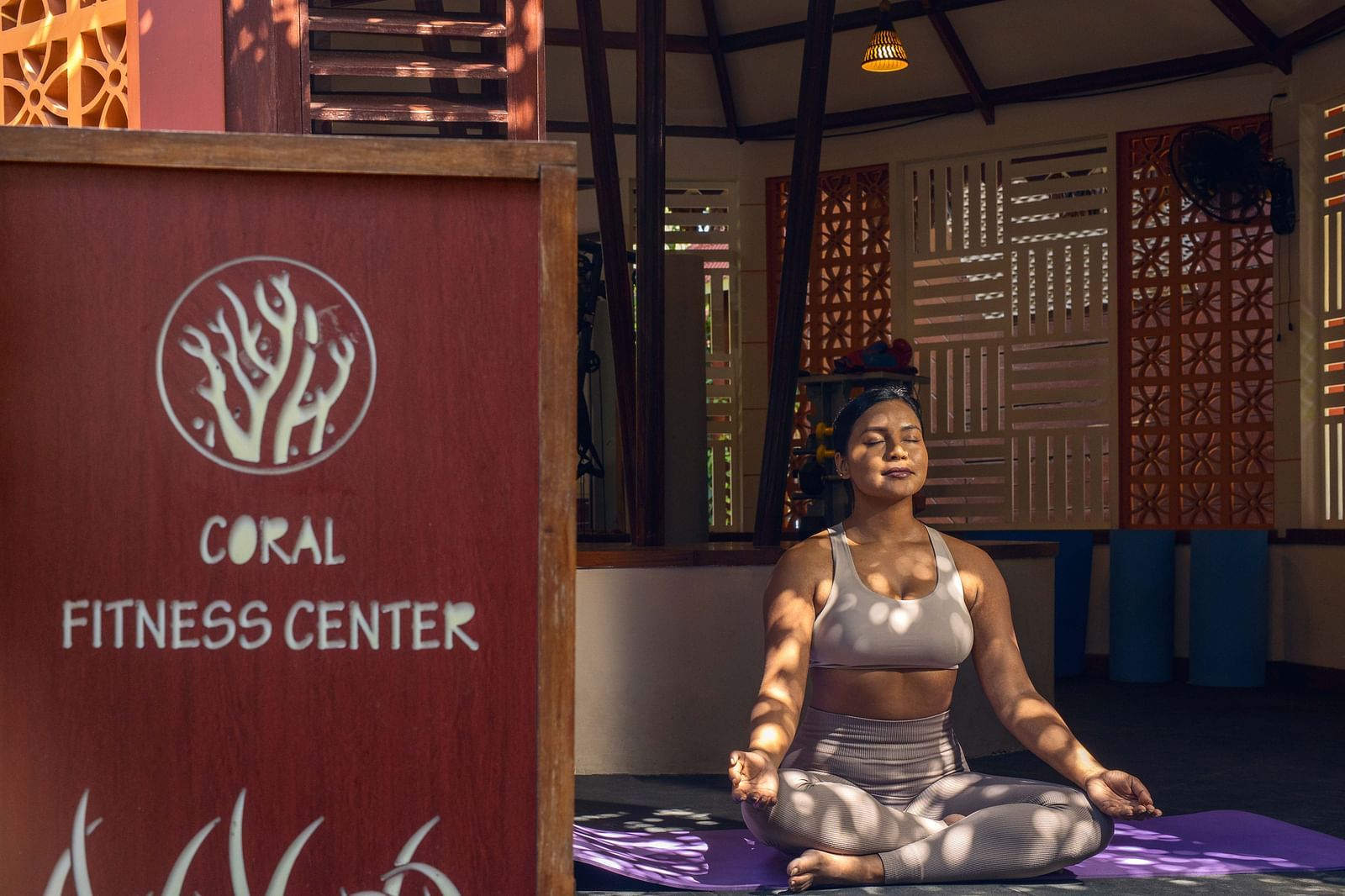 : A sign for the  Opal Fitness Center displayed alongside a statue of a person in a meditative pose. The background includes rustic wooden elements and a calm environment - Coral Reef Resort & Spa, Havelock