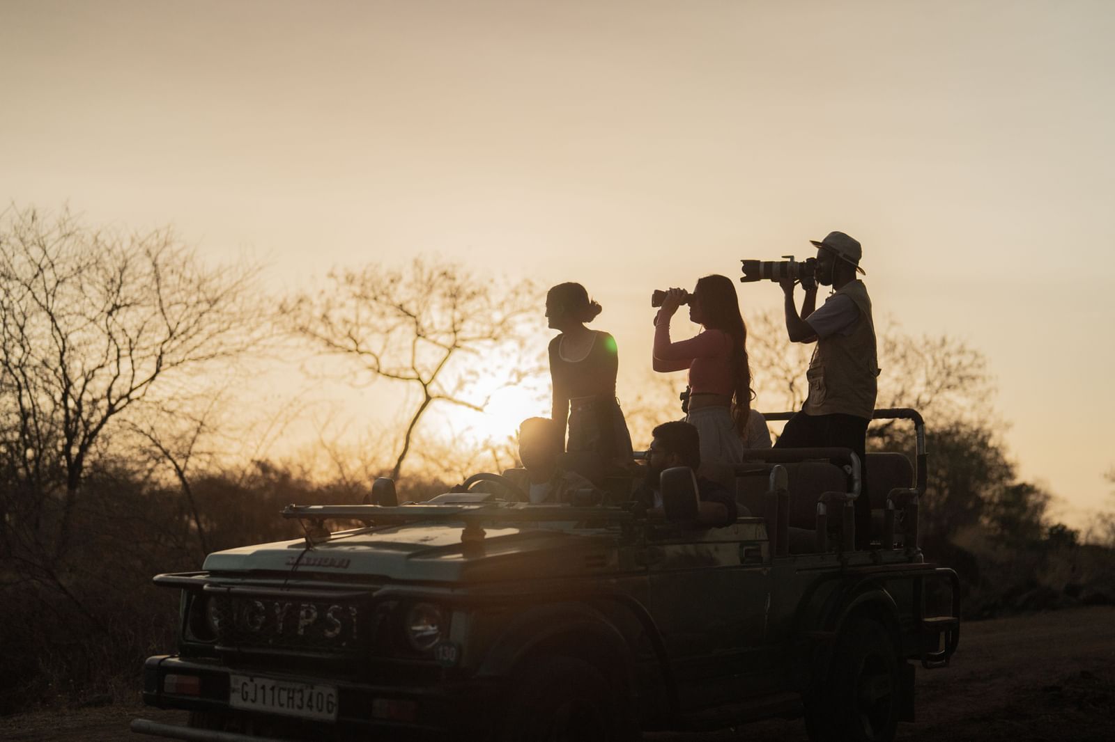 The silhouette of three people on a jeep clicking images with a camera -Daksh Eden Greenz, Sasan Gir.