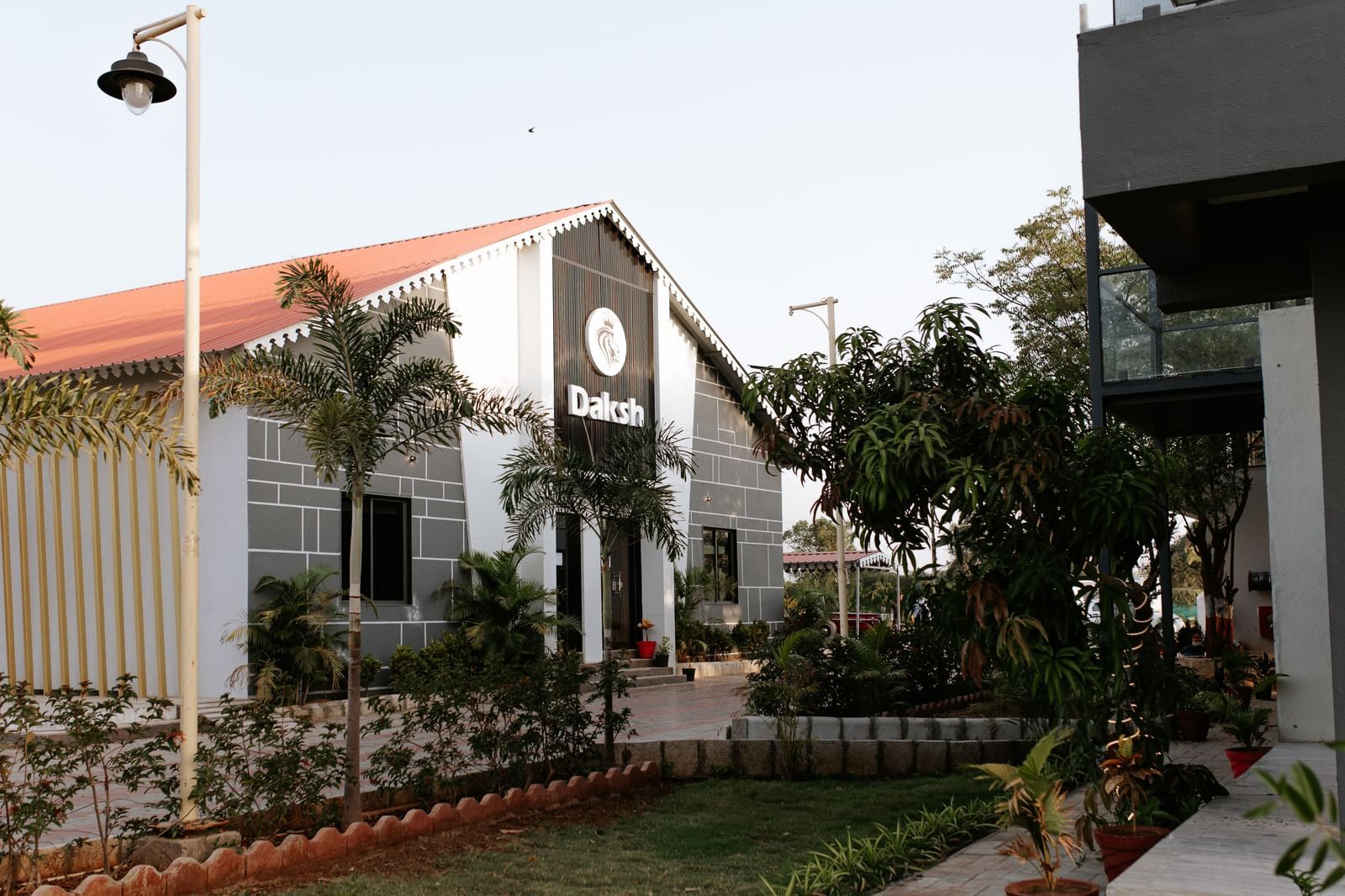 Garden view of Daksh Eden Greenz, Sasan Gir, featuring modern cottages surrounded by landscaped greenery and palm trees.