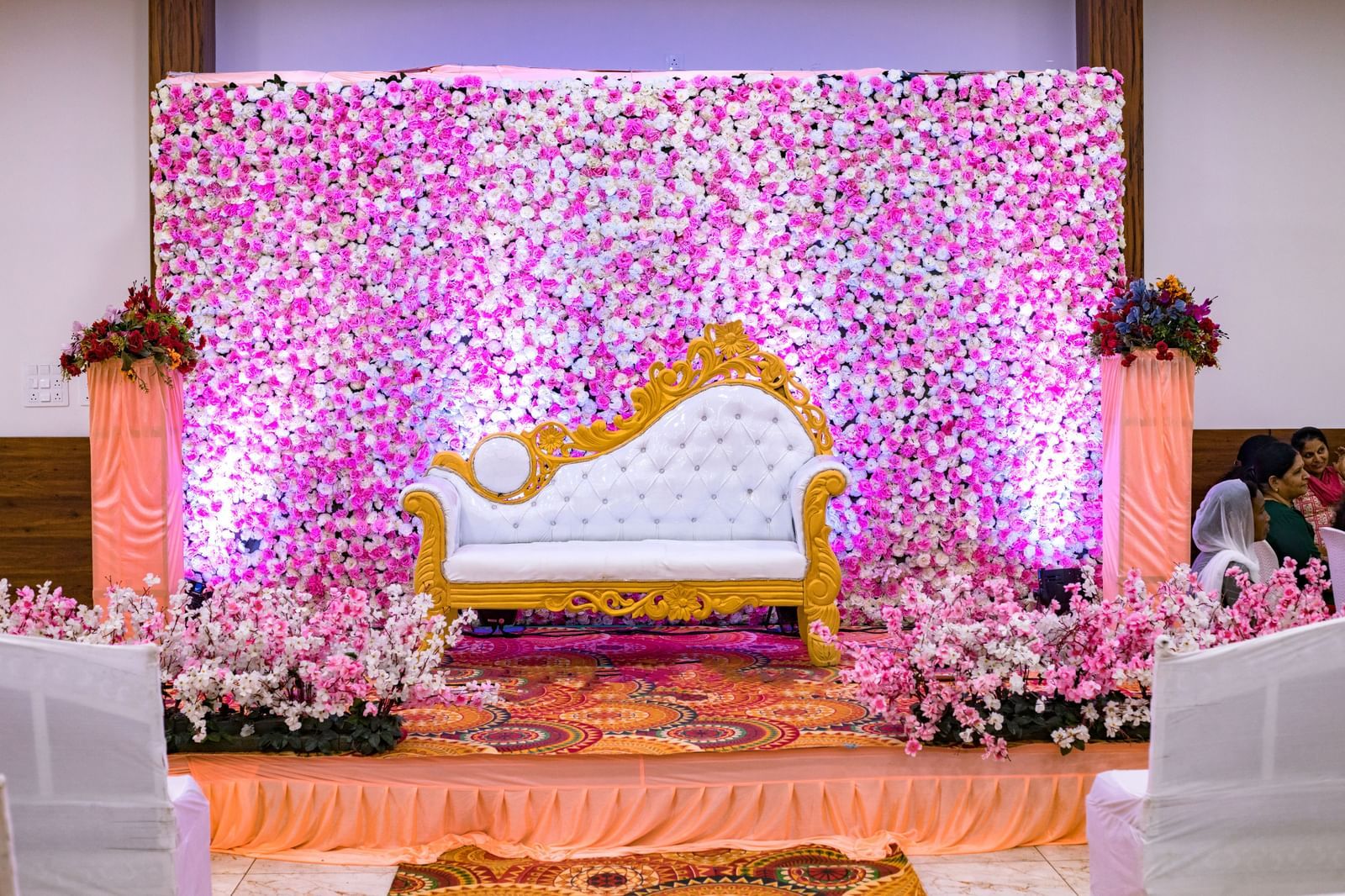 Floral wedding stage with ornate golden seating at Daksh Hotels and Resorts, set against a wall of pink and purple blooms.