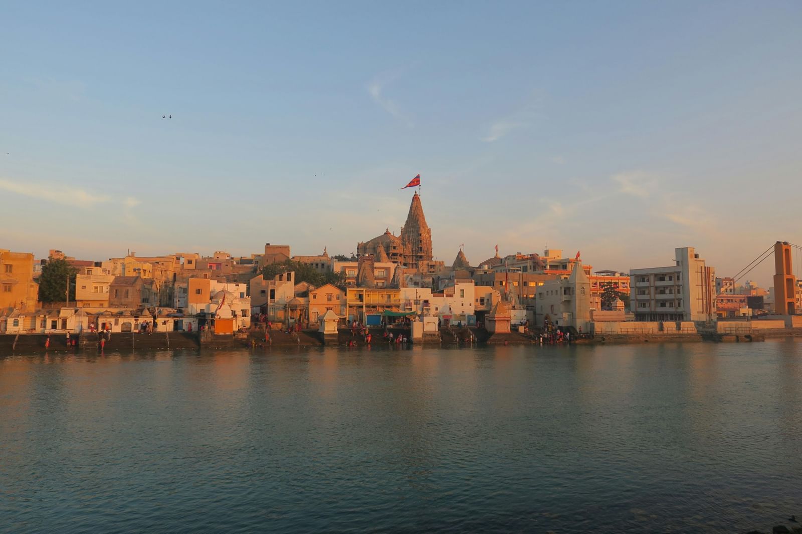 A wide angle shot of a river bank with small temples and establishment with a serene river flowing in front of them.