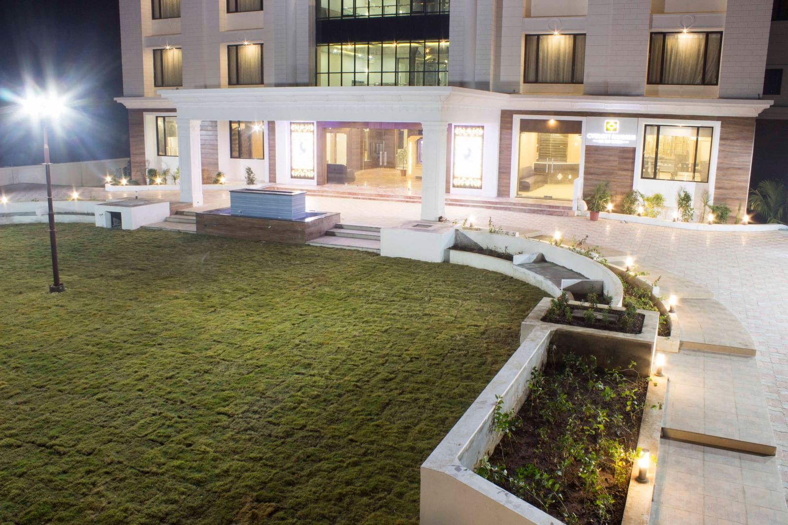 A hotel's exterior at night, showcasing its illuminated architecture and surrounding gardens | Daksh The Madhuvan Suites