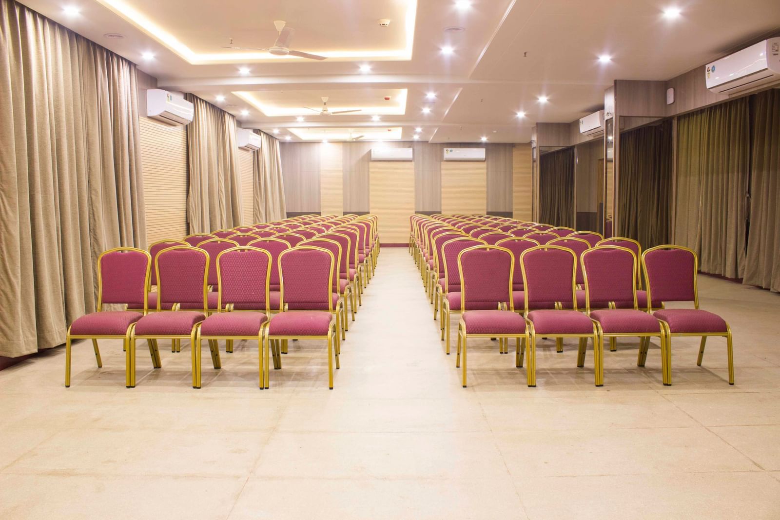 A wide shot of a banquet hall with multiple rows of empty pink and gold chairs. | Banquet Hall | Daksh The Madhuvan Suites