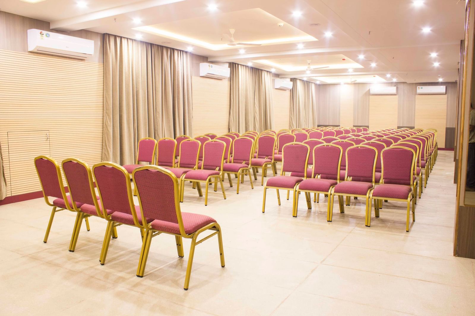 A wide shot of a banquet hall with multiple rows of empty pink and gold chairs. | Banquet Hall | Daksh The Madhuvan Suites