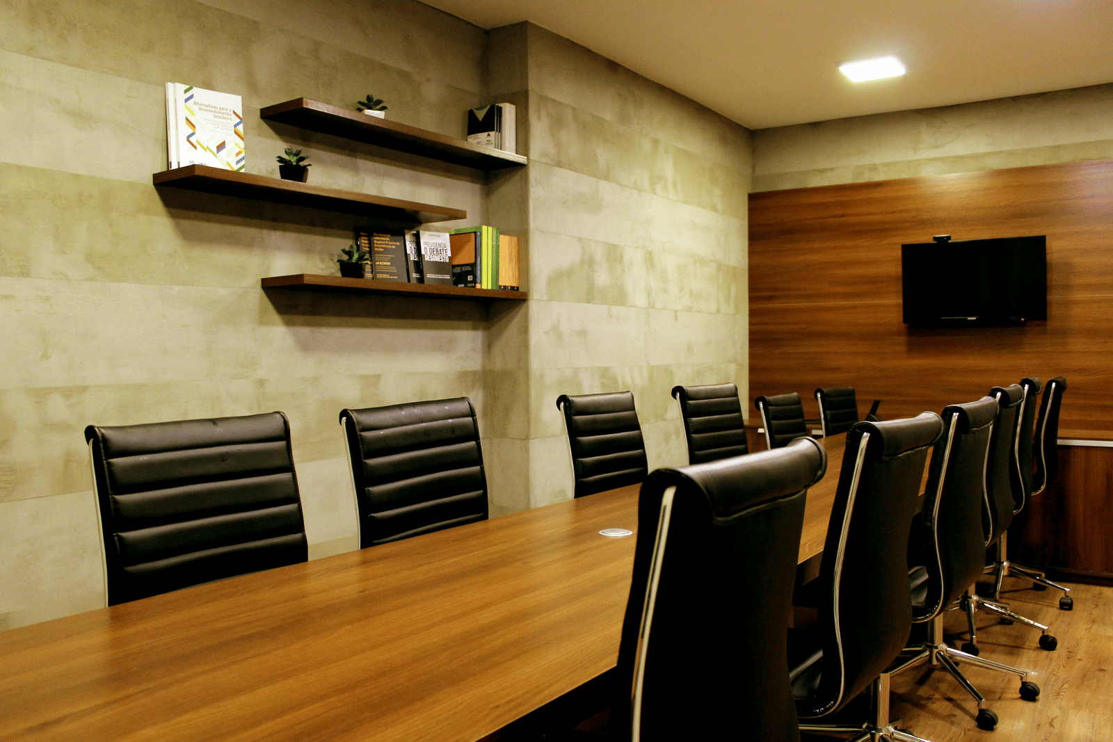A modern boardroom with a long wooden conference table, black leather chairs, wall-mounted shelves, and a television for presentations at one of the best Luxury Business Hotels in Coimbatore.