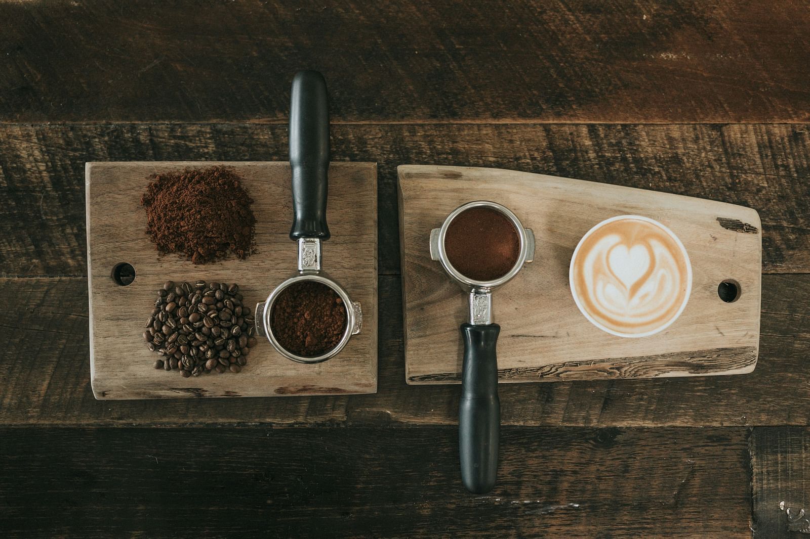Top view of two coffee portafilters kept on wooden boards, coffee beans and a cup of coffee