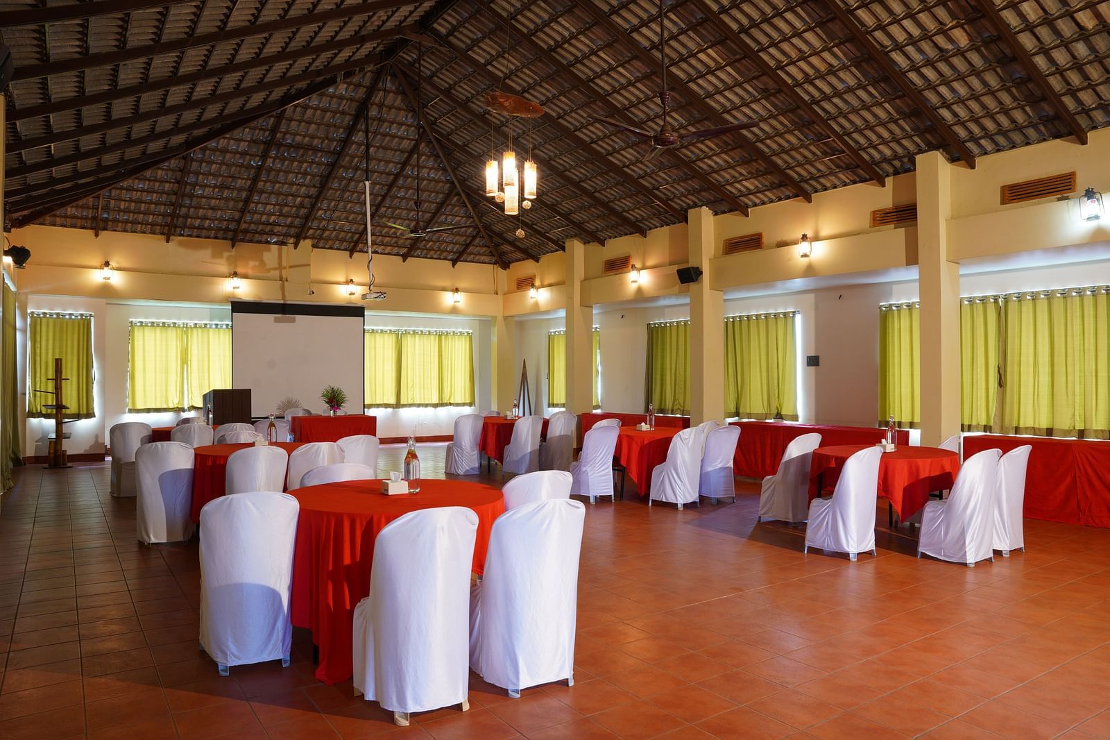 Another view of the banquet hall at Forest Escapes Koyna, showing rows of tables with red accents and white chairs.