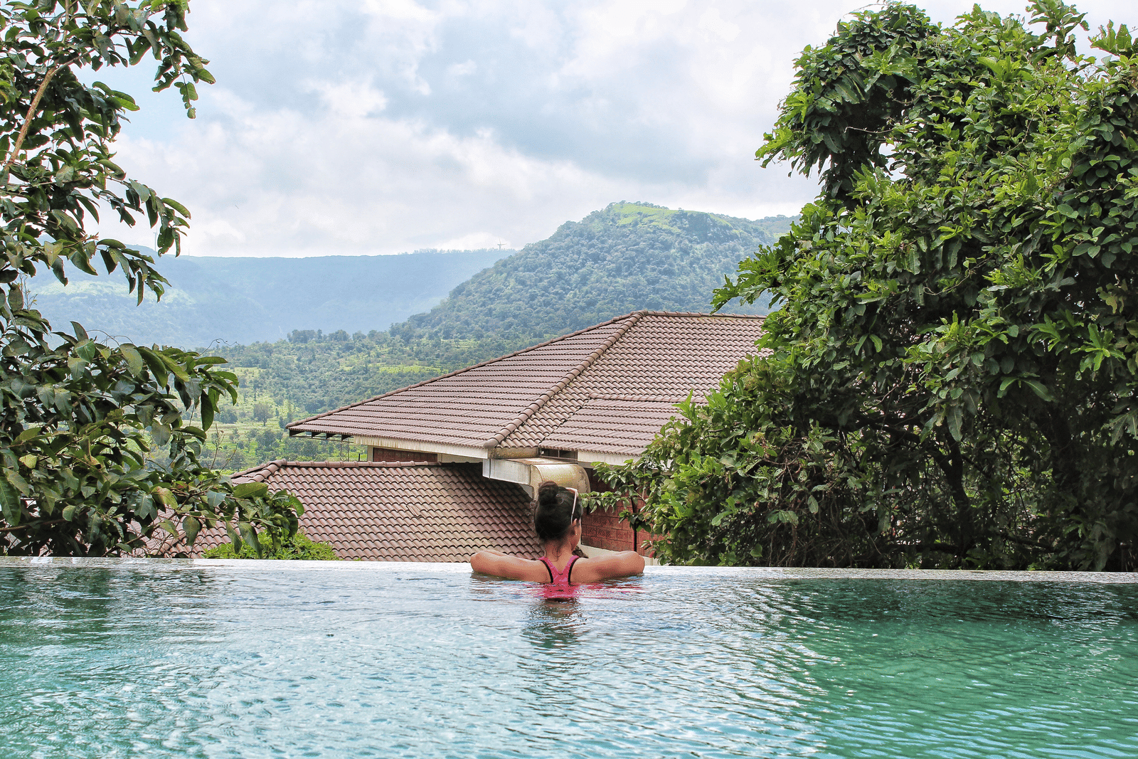 Guests at Forest Escapes Koyna relax in a swimming pool with a stunning view of the surrounding hills and greenery.