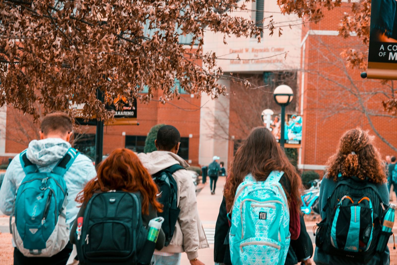 Rear view of a group of young people, wearing backpacks and walking away.