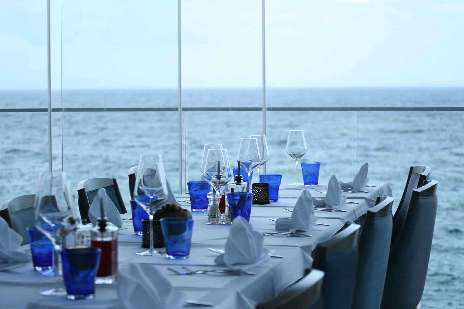 A view from inside a restaurant with a table placed next to floor to ceiling windows next to the ocean.