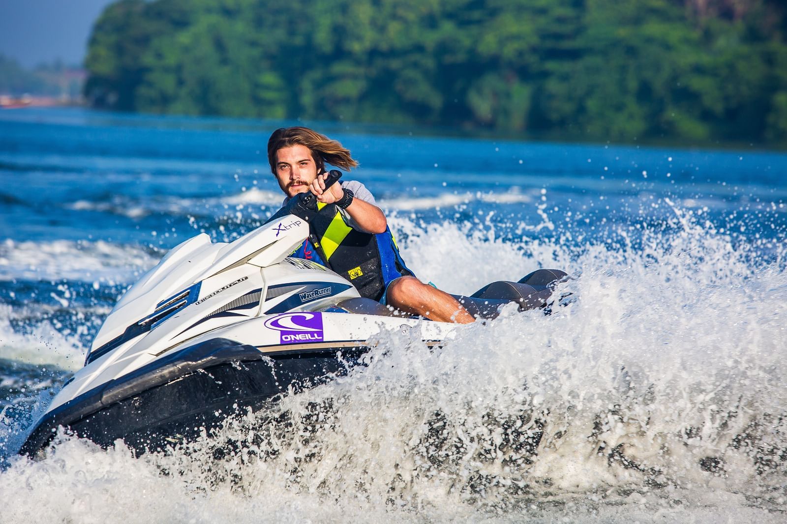 An overview of a person using a jet ski on a waterbody with greenery in the background.