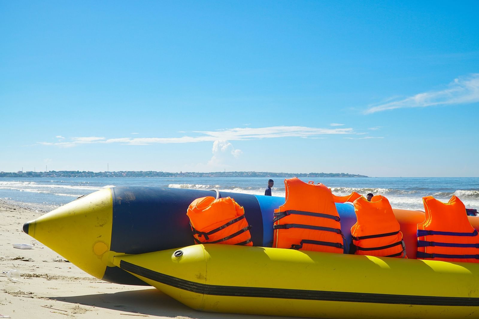 A yellow coloured banana boat with life jackets on the shore of a beach