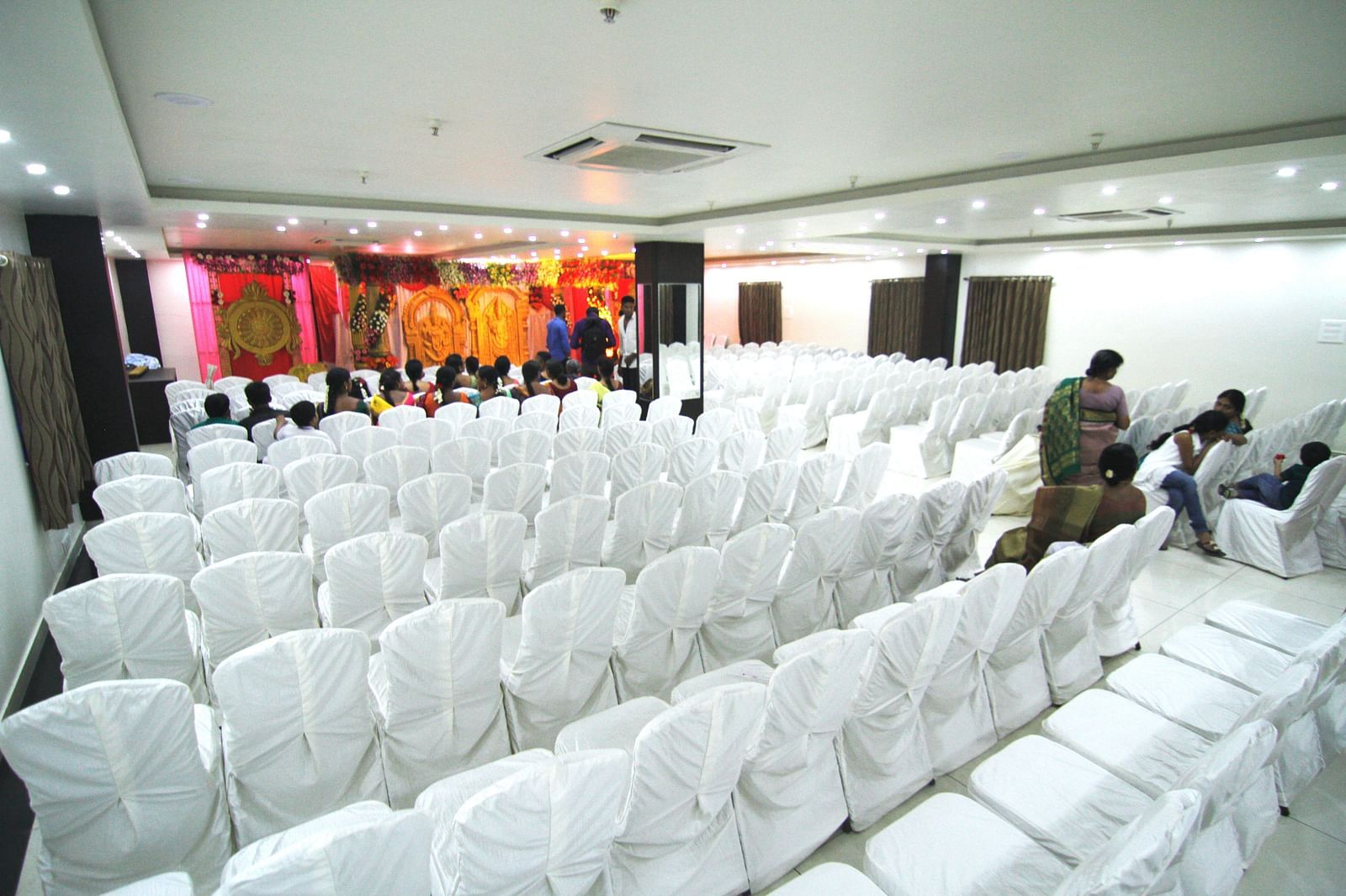 Swathi Hall with chairs neatly arranged and a decorated pulpit in front at Hotel Green Apple