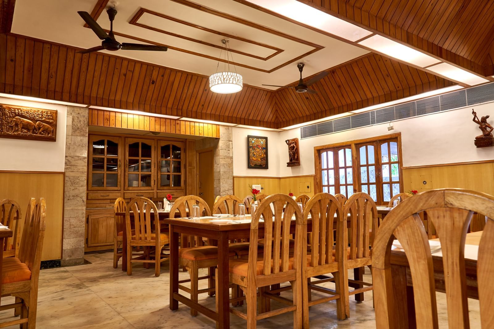 Another view of the restaurant at Hotel Mamallaa Heritage, showcasing multiple wooden dining sets and a distinctive patterned wooden ceiling.