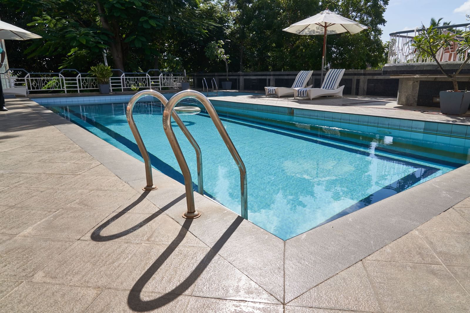 A close-up of the steps leading into the blue swimming pool at Hotel Mamallaa Heritage, with the poolside deck and lounge chairs visible.