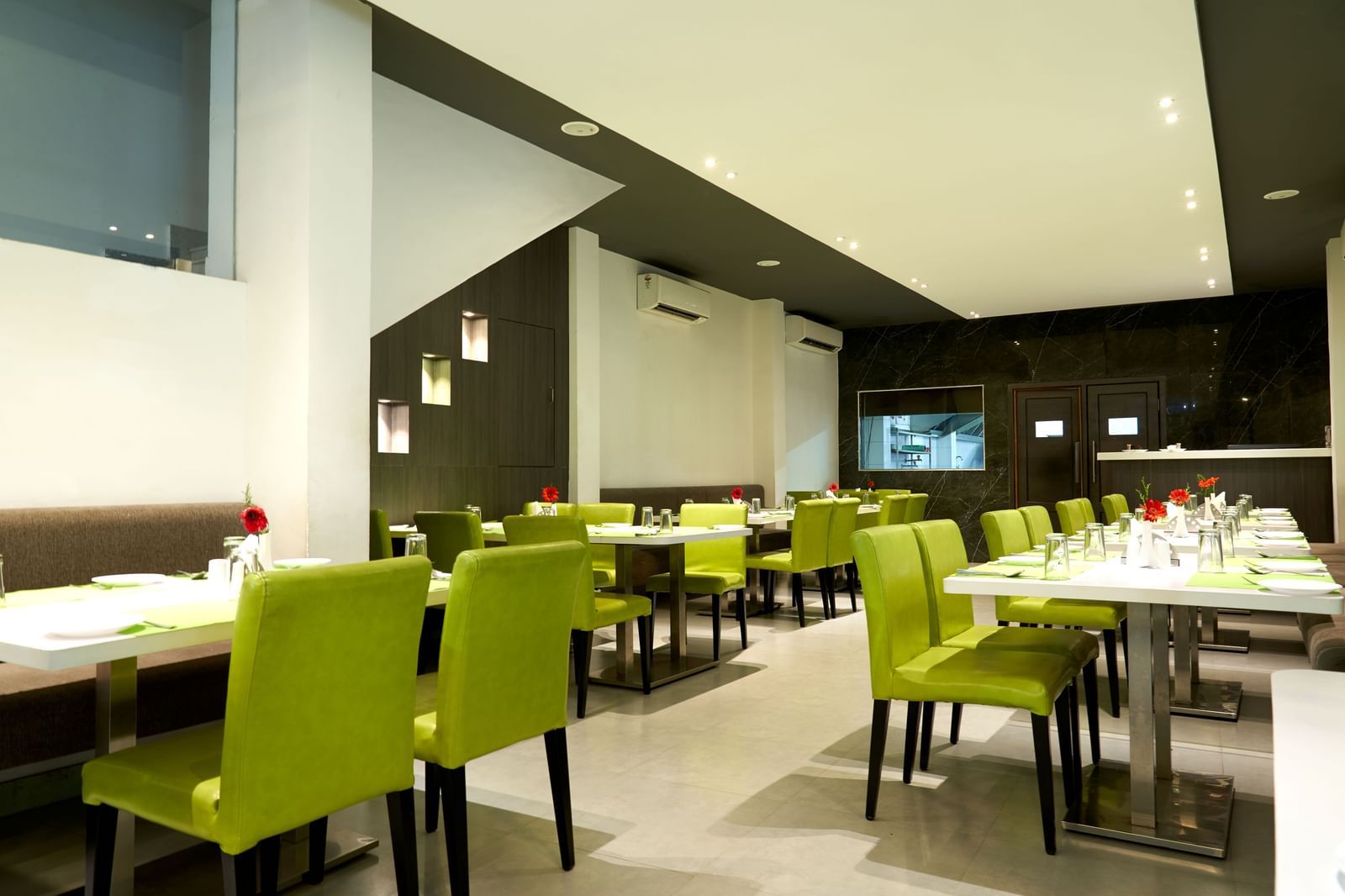 A spacious and contemporary restaurant area at Hotel Mamallaa Heritage, featuring multiple tables set with lime green chairs and white tablecloths.