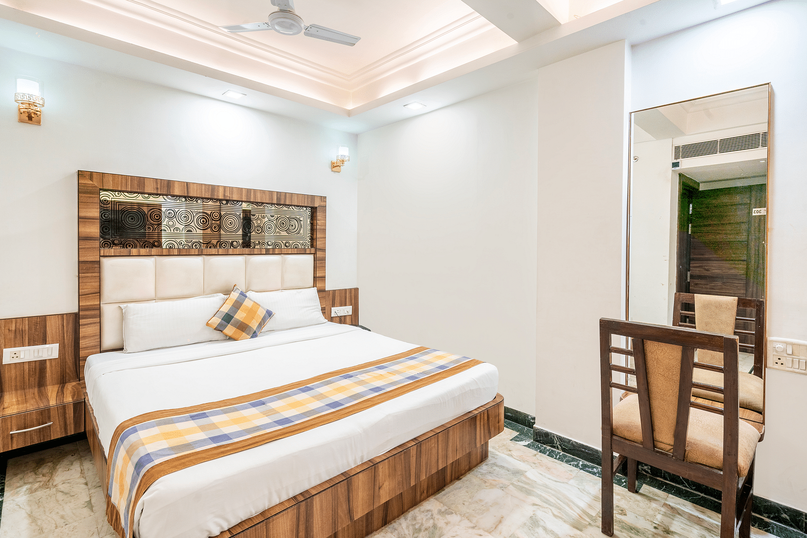 A side angle view of the bedroom at Hotel Moti Palace, featuring a comfy bed and a dressing table.