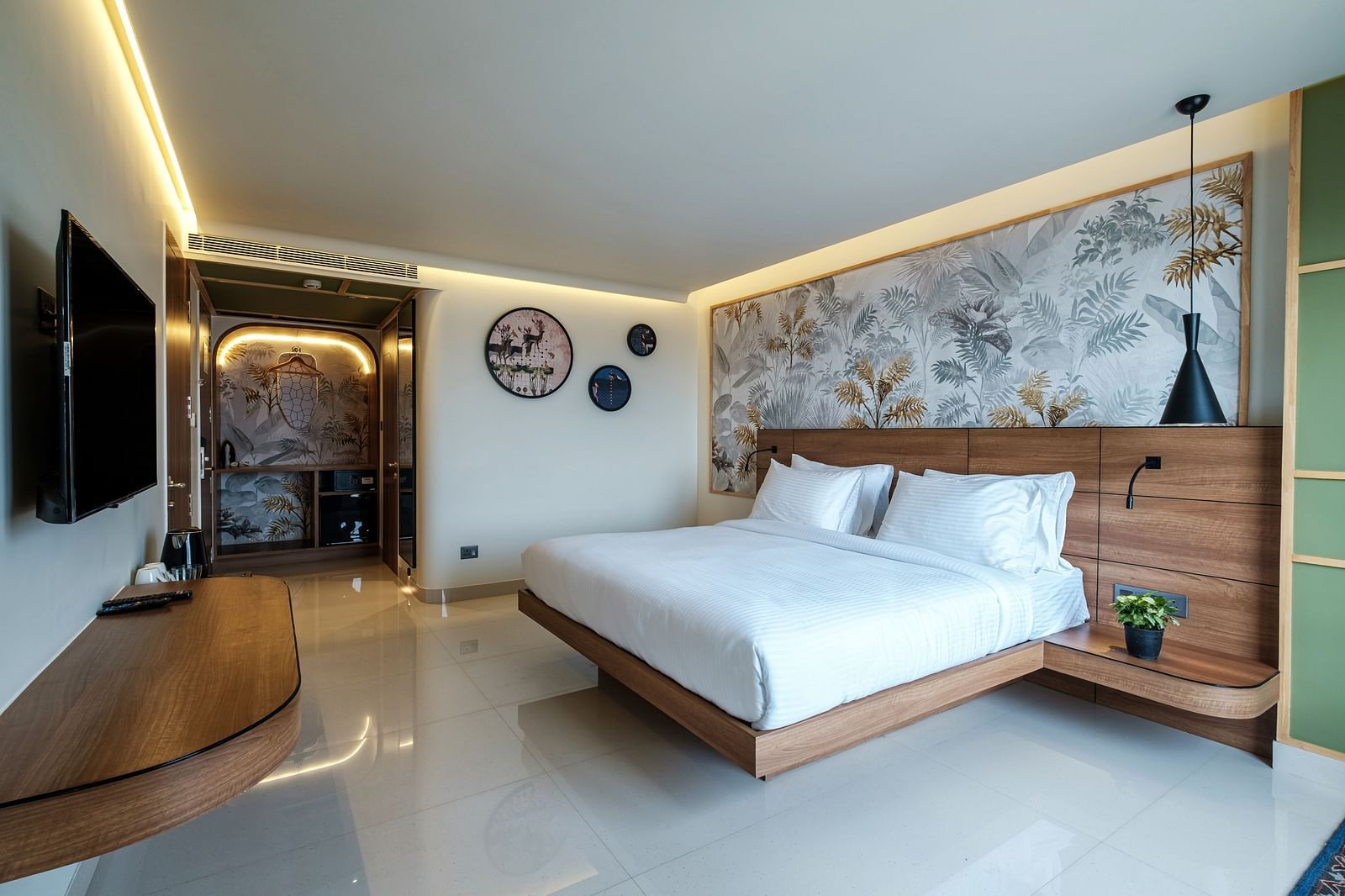 A spacious room with a large bed, opposite a wall-mounted television and a wooden table beneath it, creating a cosy and functional space at Indie Stays