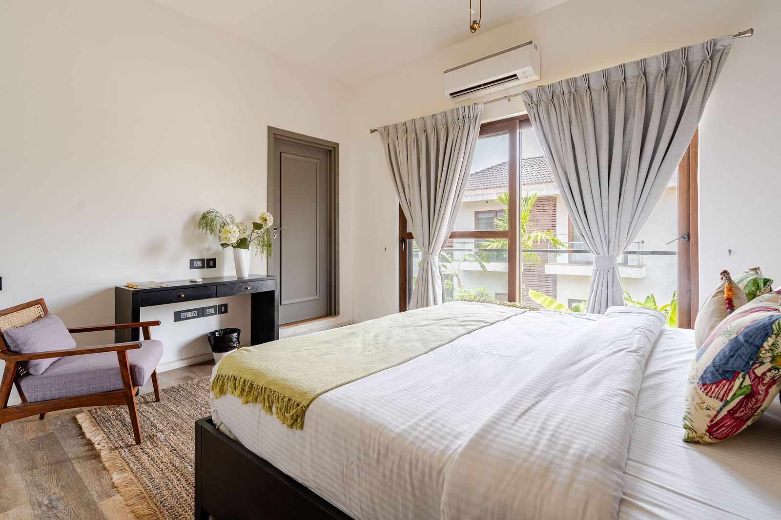Bright bedroom with a large bed, soft grey curtains, a black writing desk, and a wooden armchair on a textured rug - Lindsay Manor