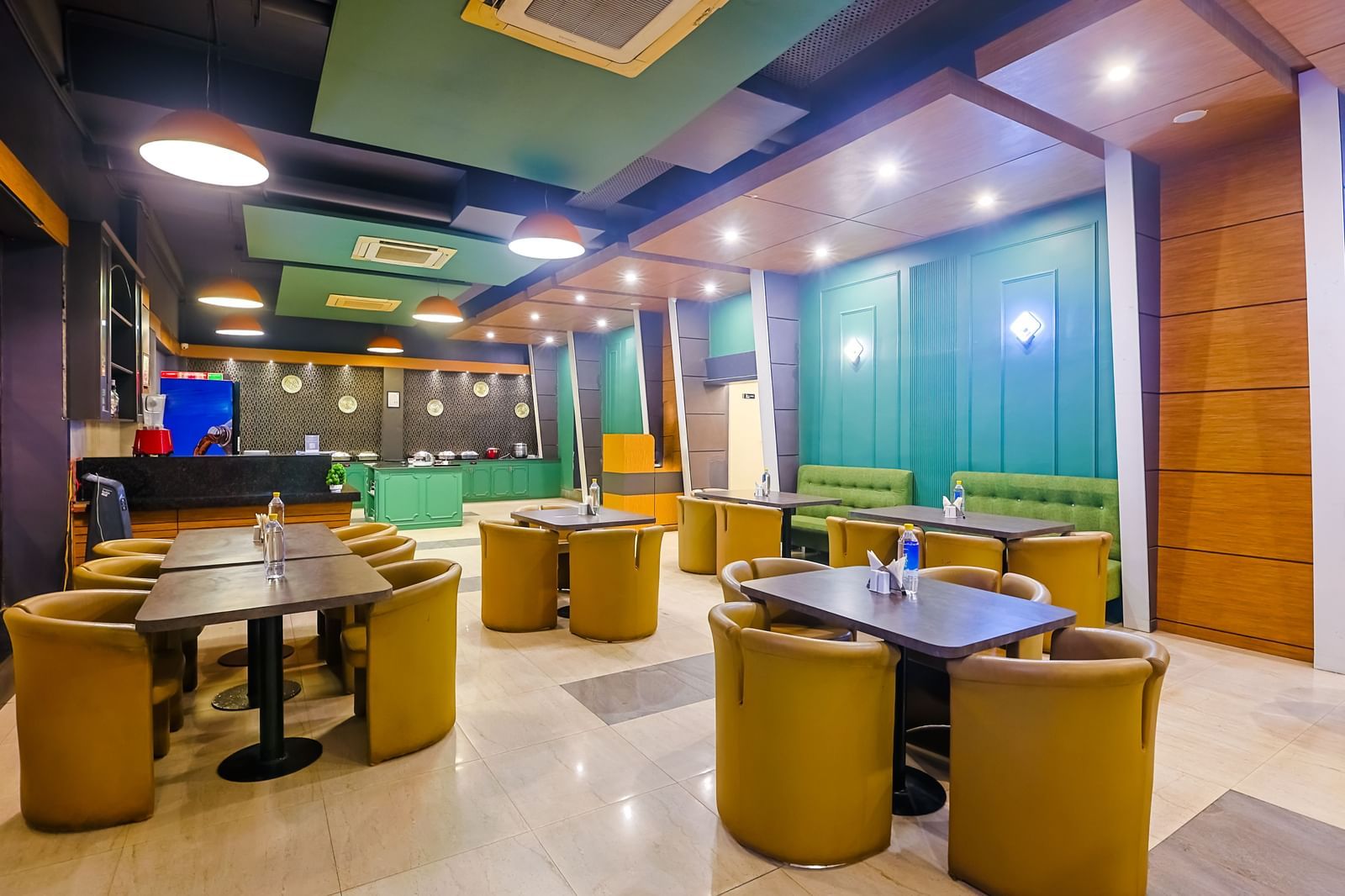 Restaurant dining area with round tables, cushioned chairs and lighting at Max Hotel Prayagraj.