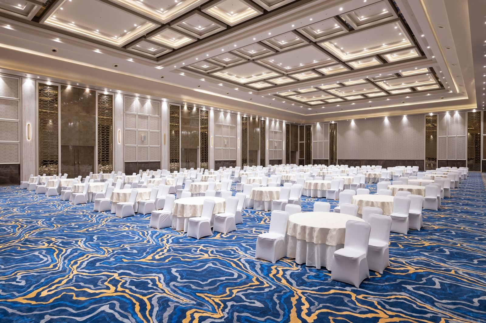 Grandis Ballroom set up with round tables and white linen seating under bright lighting at Merlis Hotel, Coimbatore