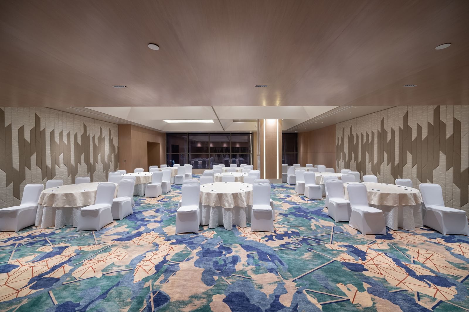 Round-table banquet setup in a spacious, well-lit function hall at Merlis Hotel, Coimbatore.