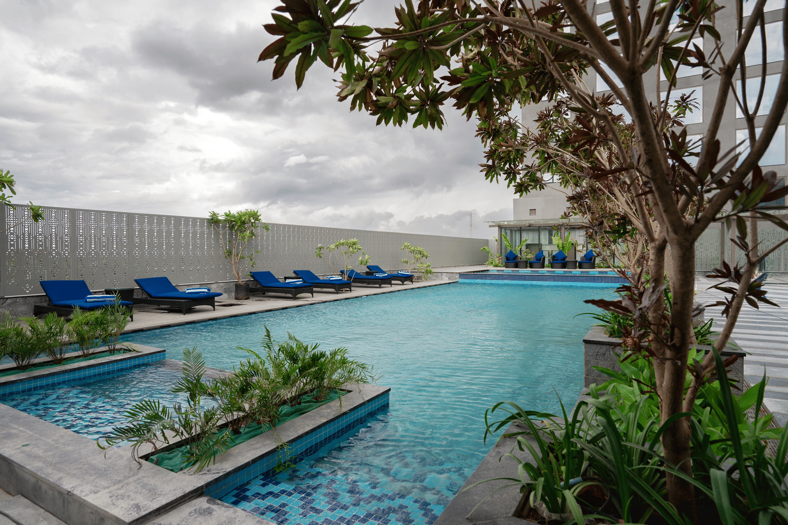 A tranquil poolside area surrounded by plants and modern design at Merlis Hotel, Coimbatore.