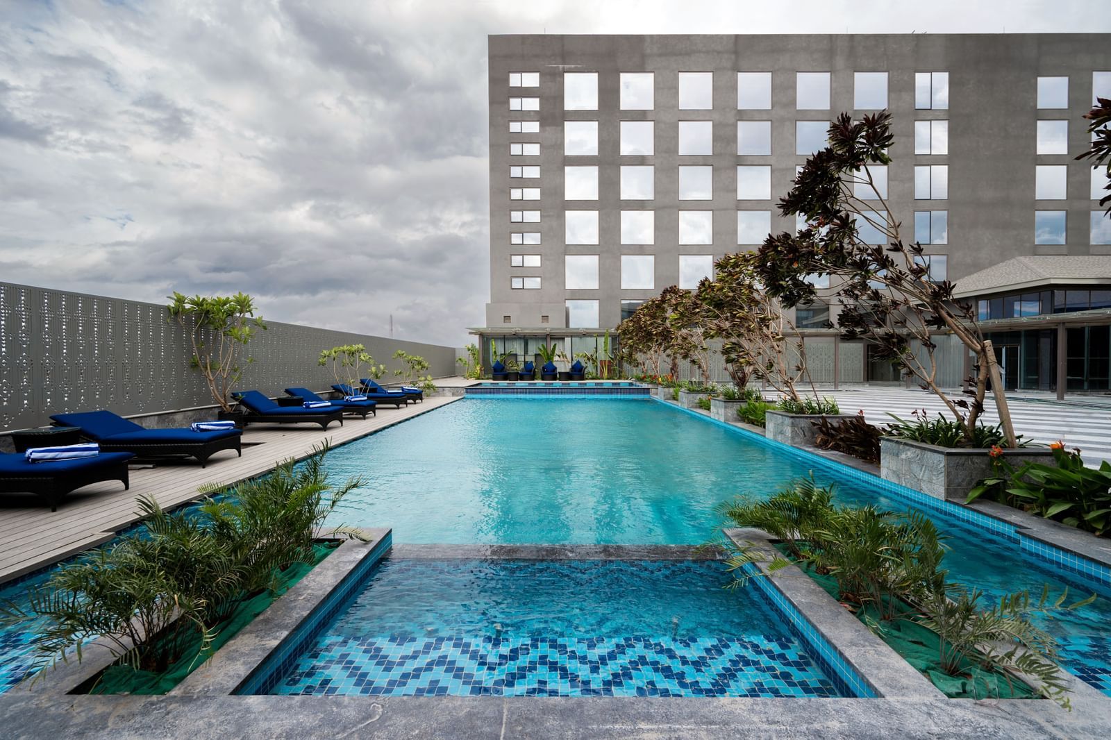 Outdoor swimming pool with city view and stylish deck chairs at Merlis Hotel, Coimbatore.