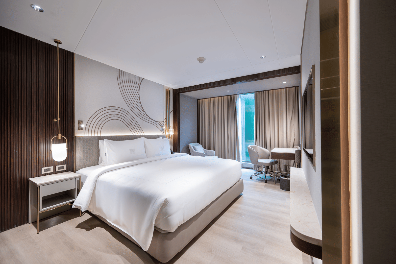  A contemporary hotel bedroom featuring a large double bed, modern lighting, and a small desk area at Merlis Hotel, Coimbatore.