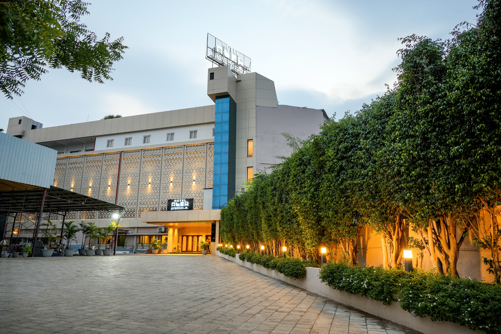 Exterior view of hotel building with driveway and trees at Pravasa Hotel, Kolhapur.