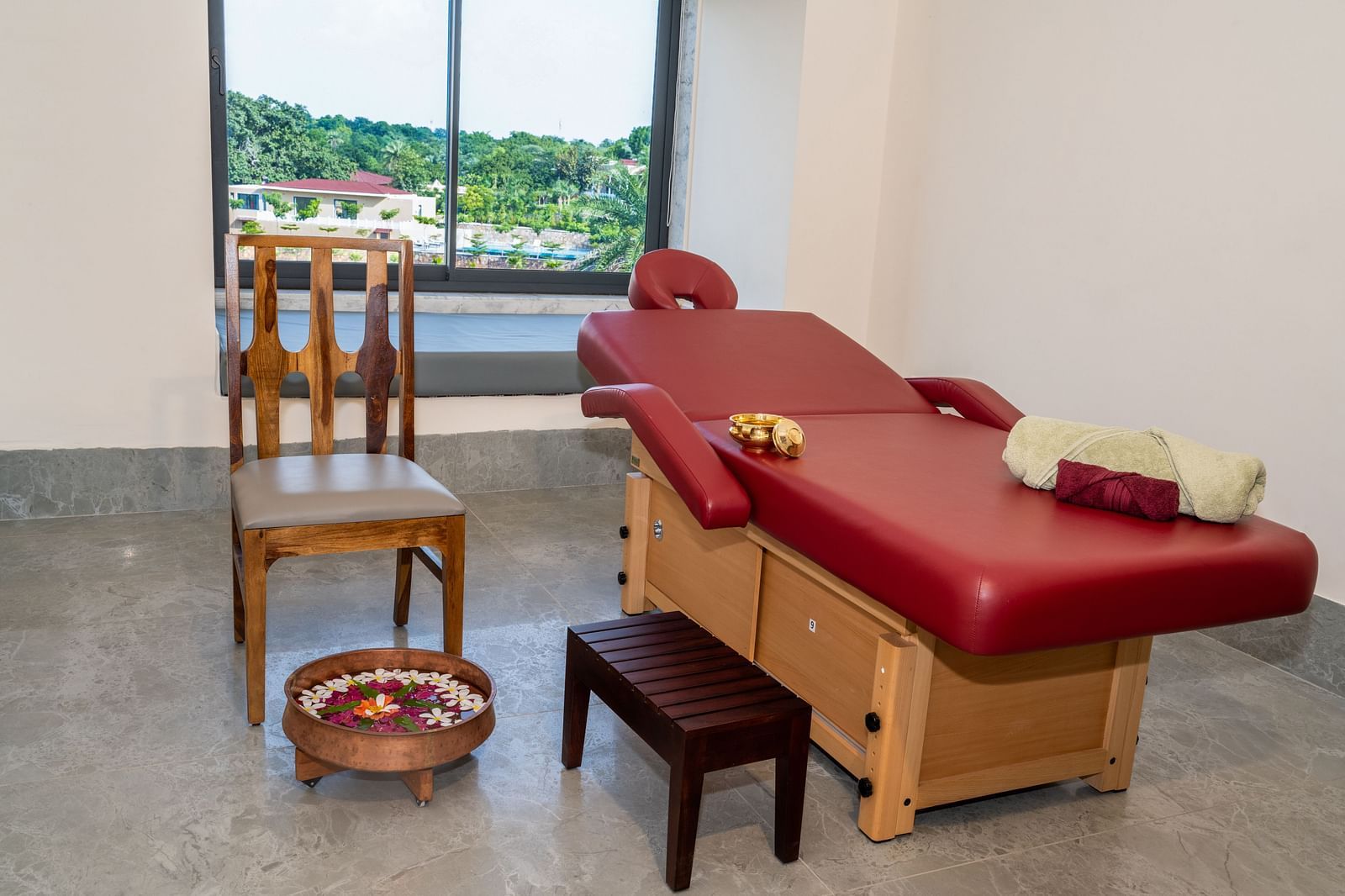 An overview of a massage room featuring a bed, a chair, a small stool, a bowl, and some spa equipment - Rajbagh Wellness.